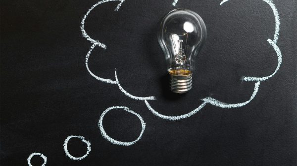 Light bulb laying on chalkboard with drawn thought bubble, symbolizing creative ideas.